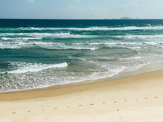Sandy seashore, calm soft waves at sea, sunny weather, blue sky with white clouds