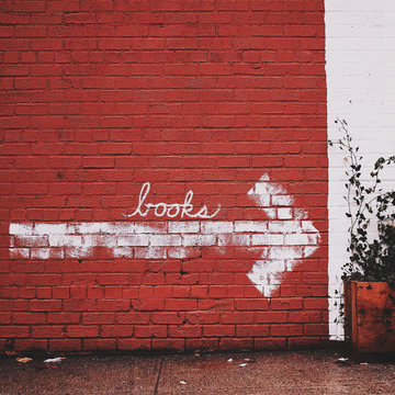 An arrow painted on a red brick wall with the word ""Books""