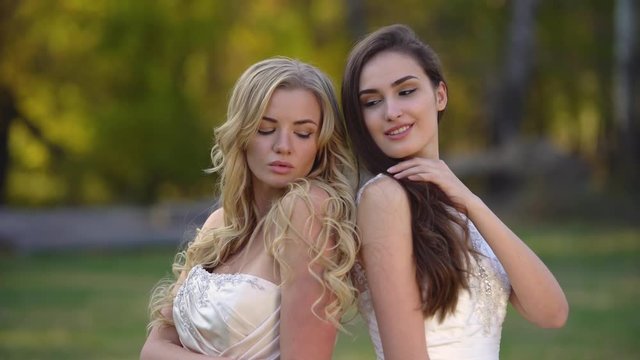 Two brides are posing in the sunshine against a beautiful landscape of autumn nature. Brunette and blonde women