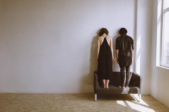 A couple standing on a sofa with a spat head to the wall. the concept of hopelessness