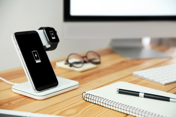 Mobile phone and smartwatch with wireless charger on wooden table. Modern workplace accessory