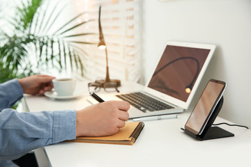 Man working at table while his mobile phone charging with wireless device