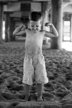 Shirtless Little Boy Flexing his Muscles on the Beach