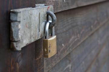 Padlock and steel hasp secure entry to a wooden shed, close up.
