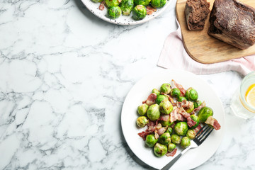 Delicious Brussels sprouts with bacon on white marble table, flat lay. Space for text