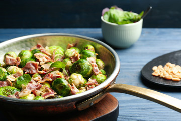 Delicious Brussels sprouts with bacon in frying pan on blue table, closeup