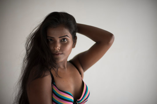 Portrait of an young and beautiful dark skinned Indian Bengali woman in colorful lingerie/bikini and hot pants posing in casual mood in white studio background. Boudoir photography.