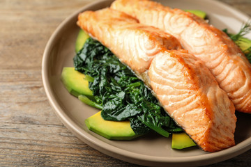 Tasty salmon with spinach and avocado on wooden table, closeup