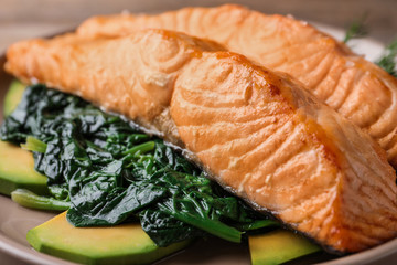 Tasty salmon with spinach and avocado on plate, closeup