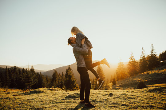 Enamored guy holding a girl in his arms, a frame at sunset. Couple enjoying sunset view from top of a mountain. Travel concept.
