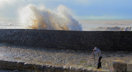 Photographer taking picture of wave splashing on The Cobb in Lyme Regis, Dorset