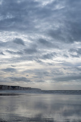 Falaises de Caux. Somme. la plage de sable à marée basse. Des nappes d'eau se sont formées sur la plage. Le ciel nuageux se reflete dans ces flaques d'eau. Les falaises en craie s'étendent à l'infini