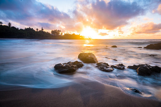 BeautifulTropical Island Paradise of Colorful Pastel Sunrise Sky at Dawn with Sun Coming Over Ocean Horizon on Sandy Beach with Smooth Water and Mountain Background and Pink Clouds on Maui Hawaii