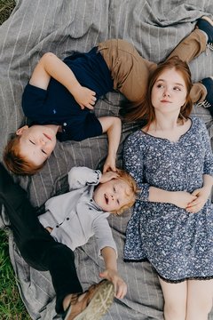 Redhead girl of 14 years old and two happy boys of 5-9 years old lying on the gray plaid in the park