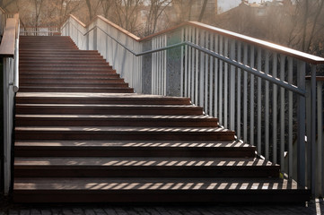 Fototapeta premium Staircase with a shadow. Close-up staircase with wooden steps and metal railing. A play of light and shadow in the evening.