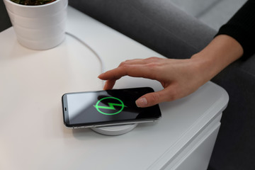 Woman taking smartphone from wireless charger in room, closeup - obrazy, fototapety, plakaty