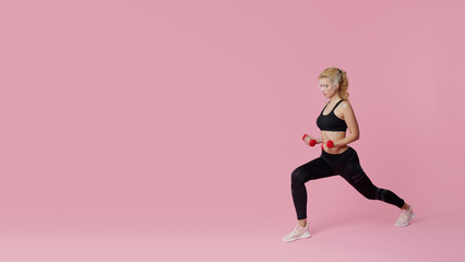 Fitness girl with perfect slim and fit body training muscles with dumbbells on pink background. Sporty woman in sportswear. Sporting goods advertising