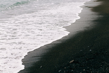 a sea wave arrives on the shore with black volcanic sand . beautiful natural background in Iceland