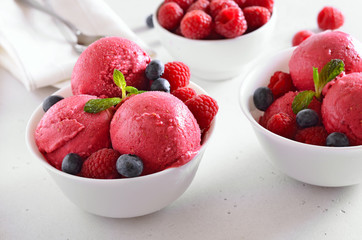 Raspberry ice cream scoop with fresh raspberries and blueberries in bowl