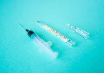 a disposable syringe, an ampoule with the drug and a body thermometer lie on a blue-green paper...