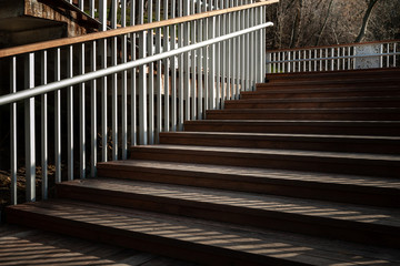 Staircase with a shadow from the railing. The rising staircase with wooden steps and metal railing. A play of light and shadow in the evening.