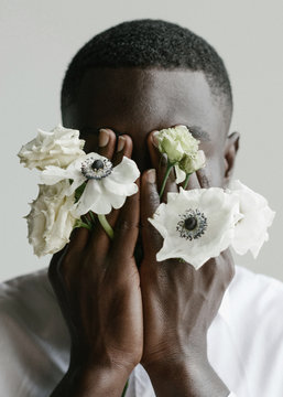 Portrait of handsome african guy who's covering his face with his arms and flowers through his fingers