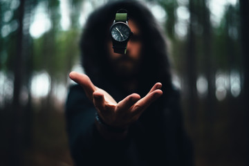 Man with Hood on with Green Watch in the Air Levitating Above His Hand in the Middle of the a Dark Moody Forest