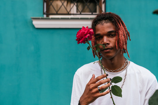 Young man dark skinned with dreadlocks and a septum piercing holding a red rouse