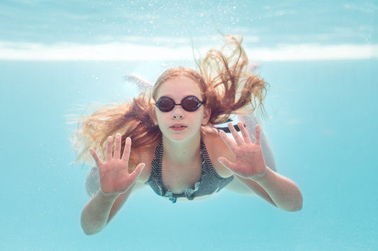 Girl underwater swimming pressing up against a glass pool wall