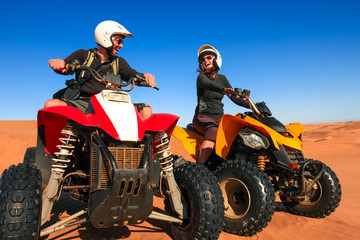 Quad driving people - happy smiling couple bikers in sand desert sunset.