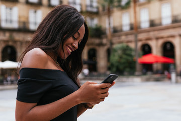 Side view of a african woman smiling and texting on her smartphone