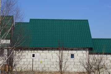 private house of white bricks with small windows under a green tiled roof against a blue sky on a sunny day