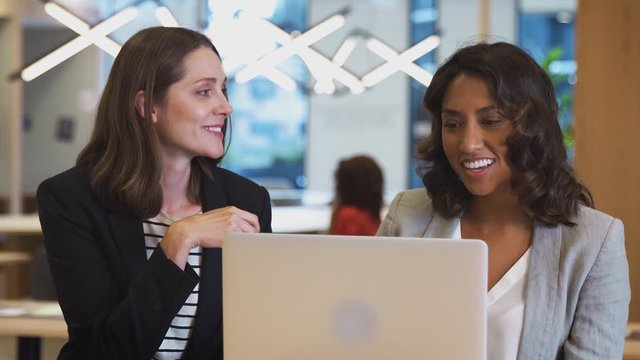 Two businesswomen with laptop at desk in open plan office collaborating on project together - shot in slow motion