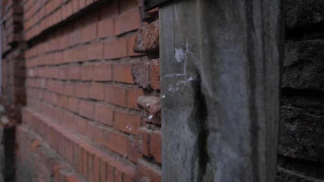 Static slow motion view of rain water flying out of a hole on a rusted, old drain pipe on the side of a red brick wall