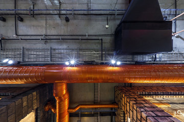 looking up on gray concrete ceiling with halogen spots and edison lamps in loft office room with air conditioning and orange ventilation pipe