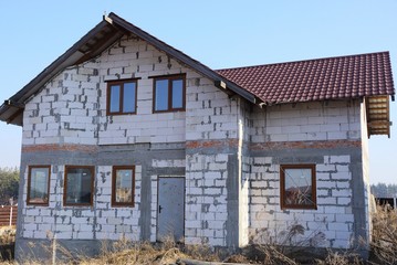 private house of white bricks with windows under a brown tiled roof on the street in gray dry grass