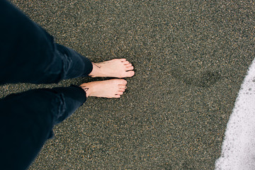 a girl stands barefoot on the wet sand on the beach. a wave washes your feet