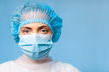 Portrait of a doctor, a young woman in a protective medical mask on her face and a cap on her head. looking seriously into the frame. on a blue background. surgeon. ambulance paramedic. copy space