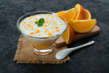  Yogurt with orange and fresh slices of orange on a black background.