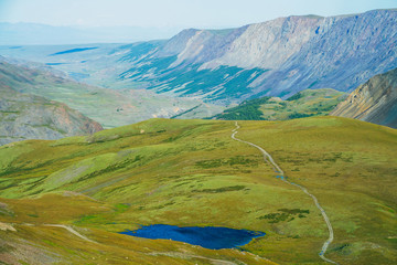 Aerial view to beautiful alpine lake with clear water and long mountain range in sunlight. Awesome landscape with vivid blue lake and green valley in distance in sunny day. Colorful highland scenery.
