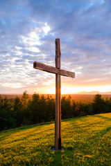 Faith Symbol Beautiful Wooden Cross on Hill with Sun Rays Behind in Nature Background Scene with Mountain Range and Colorful Sunset Sky