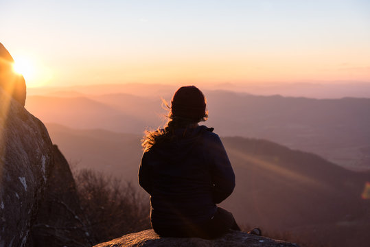 Amazing Landscape Photo With Silhouette of Woman on Hiking Adventure to Mountain Peak and Sitting on Rock Looking Out at Colorful Sunset Sky and Rolling Hills in Virginia with Sun Rays  - Powered by Adobe