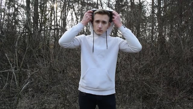 A young man in a white jacket stands against the gray nature of dry branches
