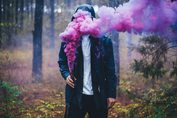 Colorful Abstract Photo Concept Idea with Man Holding Smoke Bomb with Pink Purple Blue Smoke Covering His Face Inside Damp Wet Moody Forest Scene 