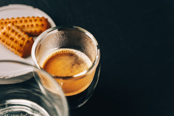 One portion of espresso in glass transparent cups,bisuits and water on a dark stone background,copy space