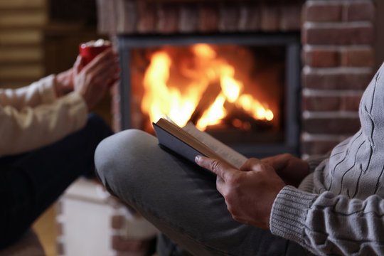 Man reading book and his girlfriend near burning fireplace at home, closeup