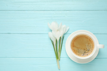 Cup of morning coffee and crocuses on light blue wooden table, flat lay. Space for text