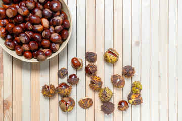 Composition of half-opened chestnuts in prickly shell and peeled nuts in bamboo plate on light wooden background with copy space. Top view