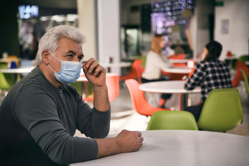 Senior man with medical mask in cafe. Virus protection