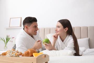 Obraz na płótnie Canvas Happy couple in bathrobes having breakfast on bed at home